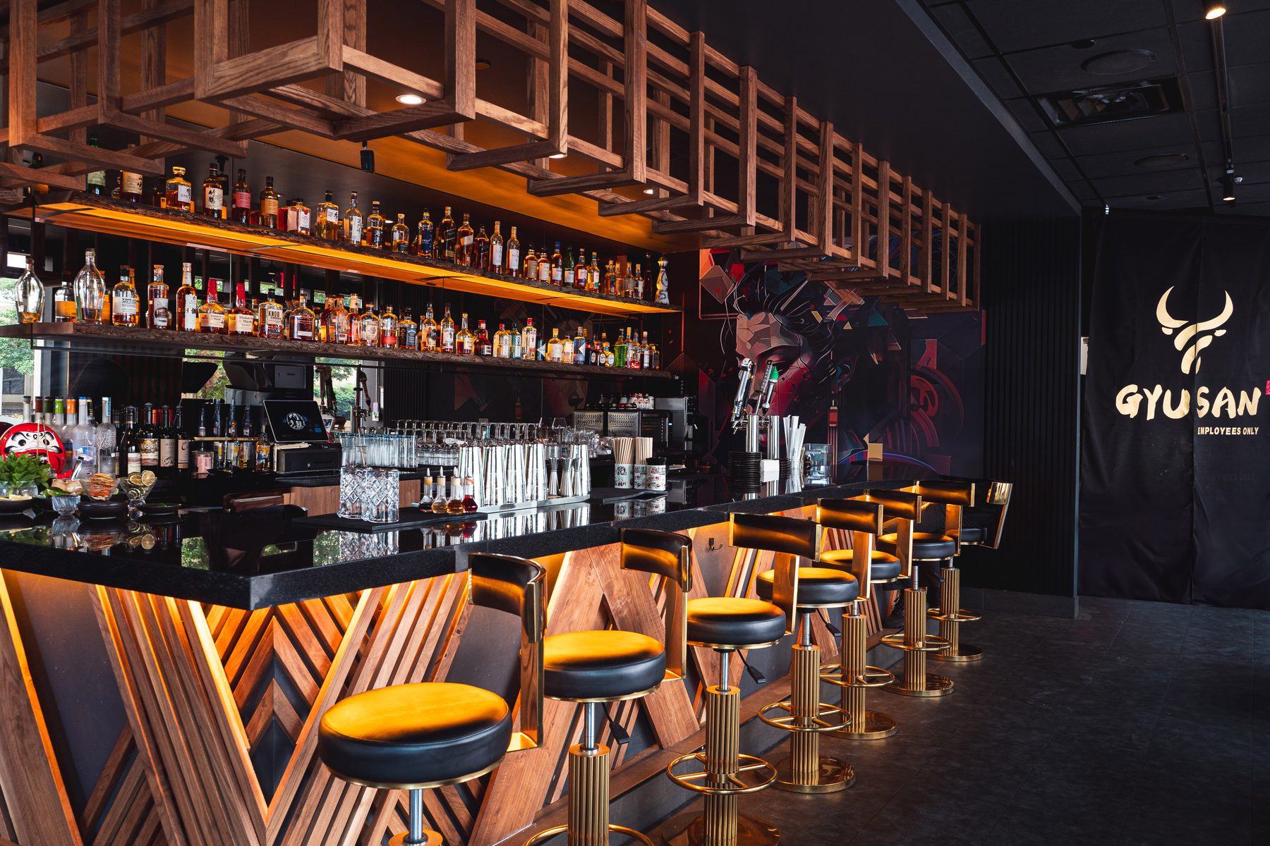 Gyusan's bar in Ballston with a lit chevron wood front, black-and-gold stools and a geometric geisha mural
