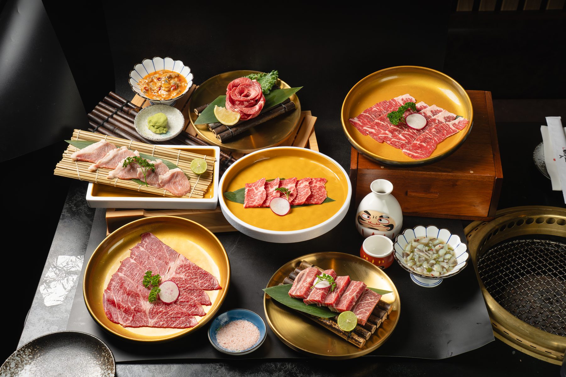 Marbled raw Wagyu slices on gold plates and bamboo mats around a brass tabletop grill at Gyusan in Arlington, VA