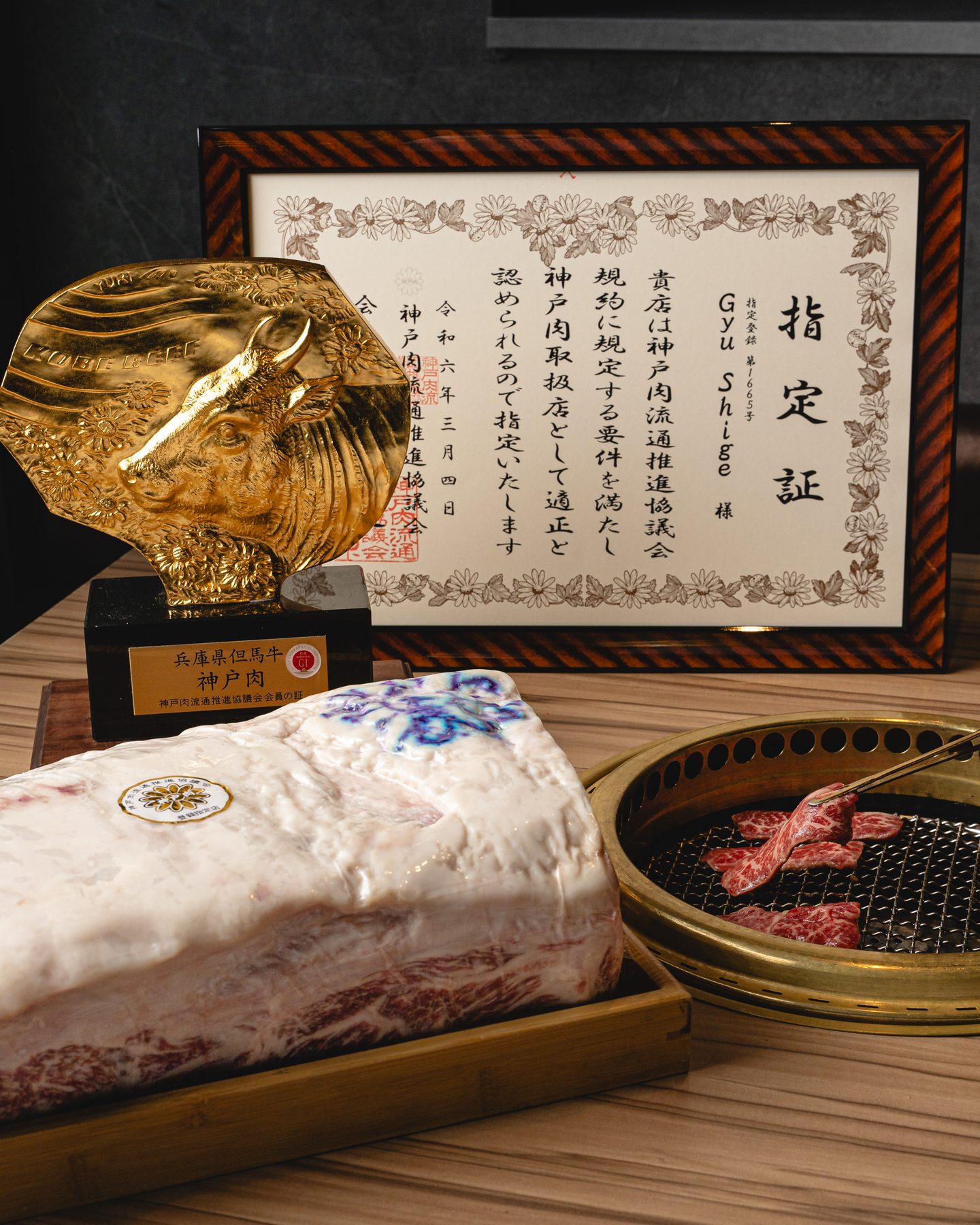 A framed Kobe beef certificate, a gold Kobe Beef trophy and a block of marbled Kobe beef beside a tabletop grill at Gyushige