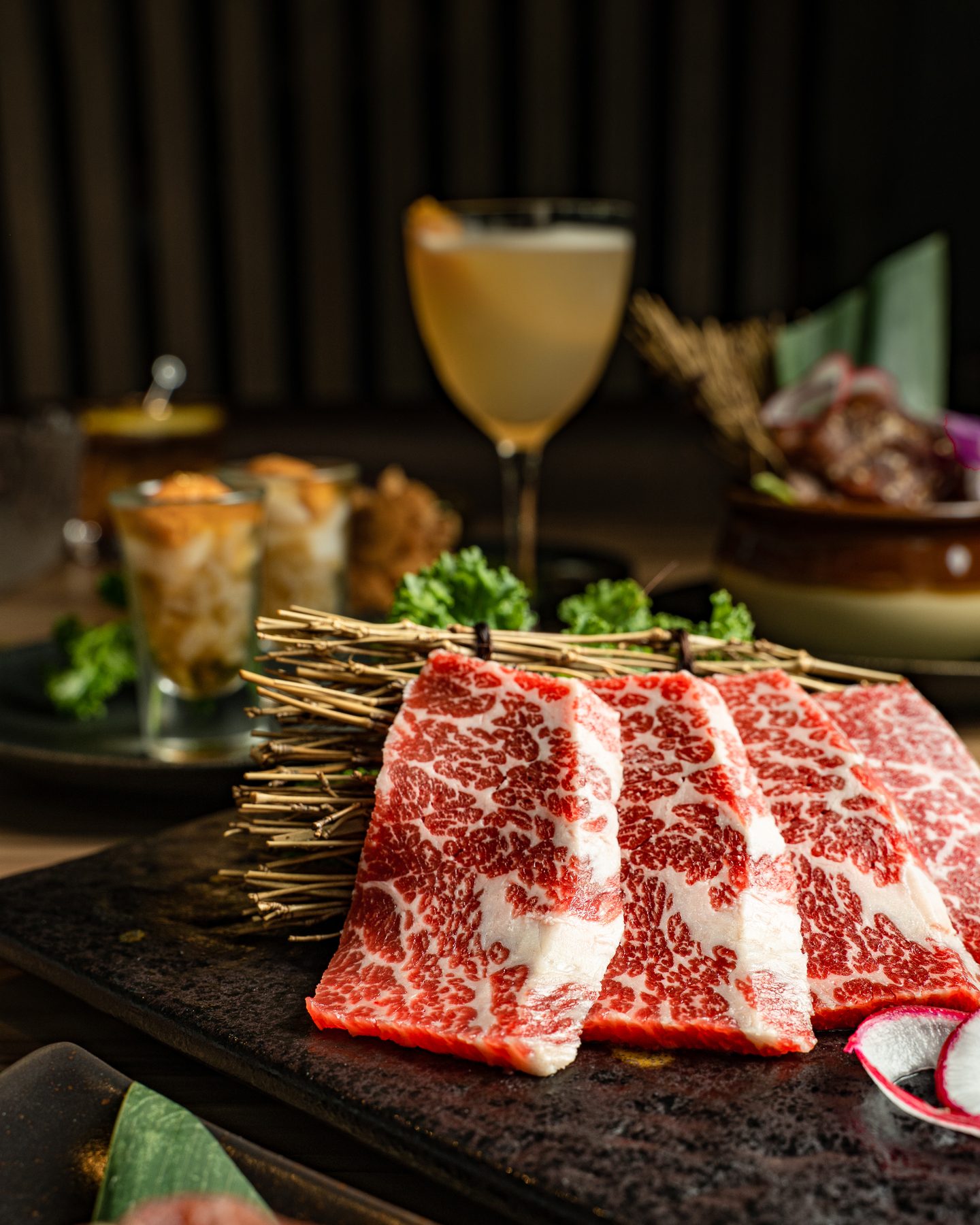 Thick slices of marbled raw Wagyu propped against a bundle of twigs on a dark stone slab at Gyushige in Fairfax, VA