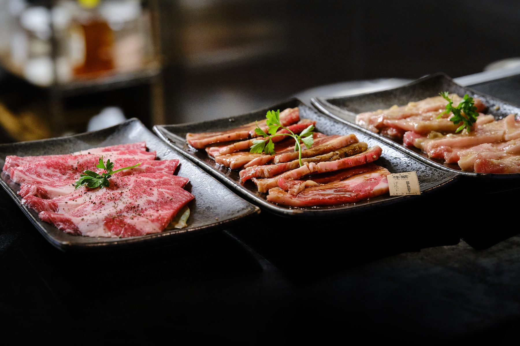Three plates of raw yakiniku beef, each topped with parsley, lined up for the grill at Gyushige