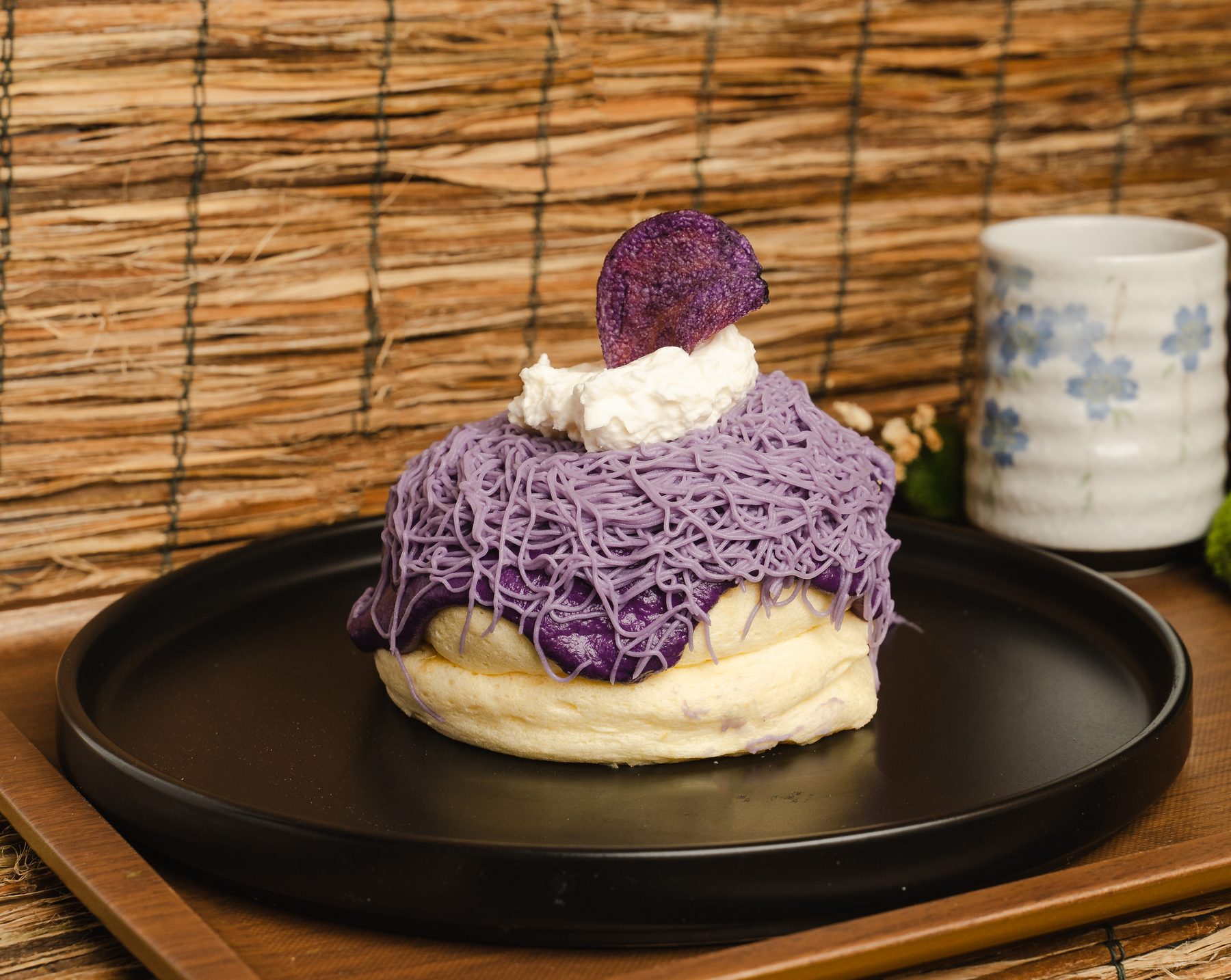 An ube soufflé pancake covered in piped purple ube strands, whipped cream and a purple sweet-potato chip at Okaeri